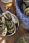 Steamed clams in a white wine broth with garlic and herbs on wooden surface — Stock Photo