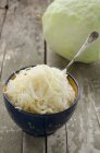 A bowl of sauerkraut with a fresh white cabbage in the background — Stock Photo