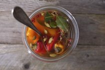 Marinated peppers in glass pot  over wooden surface — Stock Photo