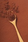 Closeup top view of cocoa powder on wooden spoon and brown surface — Stock Photo