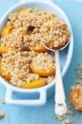 Closeup view of apricot crumble with spoon in baking dish — Stock Photo