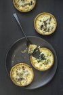 Mini spinach and mushroom quiches on black plate over black wooden surface — Stock Photo