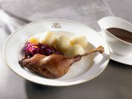 Гусиная нога с красной капустой, пельмени и соуса на белой тарелке — стоковое фото