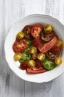 Різні кольорові скибочки помідорів на білій тарілці — стокове фото