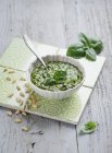 Elevated view of Pesto in white bowl with spoon, leaves and peanuts on tiles — Stock Photo