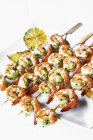Closeup view of grilled prawn skewers with herbs on white platter — Stock Photo