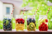 Nahaufnahme von vier fruchtigen Getränken in Schraubgläsern auf einem Gartentisch — Stockfoto