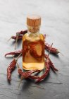 Chilli oil in small bottle over grey wooden surface — Stock Photo