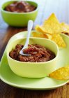 Spicy courgette salsa with tortilla chips in green bowl over plate — Stock Photo