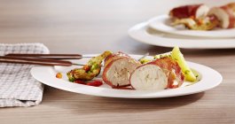 Stuffed chicken breast wrapped in ham  on white plate over wooden surface — Stock Photo
