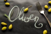 Scattered olives and a fork around the work 'Oliven' — Stock Photo