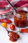 Ketchup de tomate casero en una cuchara y en un frasco flip-top sobre una superficie blanca - foto de stock