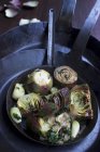 Artichokes with herbs and garlic in a hand-forged iron pan — Stock Photo
