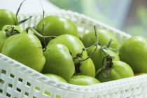 Green tomatoes in plastic basket — Stock Photo