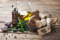 An arrangement of porcini mushrooms, oil, parsley, garlic and pepper on wooden surface — Stock Photo