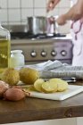 Pommes de terre nouvelles et échalotes dans une cuisine et homme flou sur fond — Photo de stock