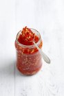 Pickled chillies in jar with spoon over white wooden surface — Stock Photo