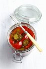 Poivre mariné et jalapeno dans un bocal en verre avec fourchette sur surface blanche — Photo de stock