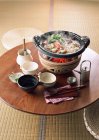 Повышенный вид на парящее овощное блюдо на углях и посуда на деревянном азиатском столе — стоковое фото