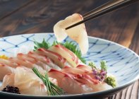 Closeup view of sea bream Sashimi with herbs and chopsticks — Stock Photo
