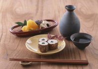 Japanese appetizer and sake over wooden surface  with wooden sticks — Stock Photo