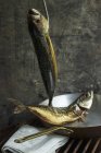 Pescado de caballa ahumado colgado de un gancho y en una sartén de cobre - foto de stock