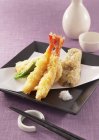 Closeup view of assorted tempura on paper and square black plate — Stock Photo