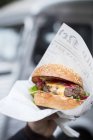 Рука держит гамбургер в бумаге — стоковое фото