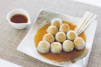 Taro dumplings with a sweet soy glaze on white plate with wooden sticks — Stock Photo
