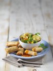 Mini spring rolls and vegetable soup on a plate over wooden surface — Stock Photo