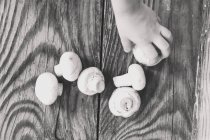 Обрізаний вид зверху руки, що збирає гриби з дерев'яної поверхні — стокове фото