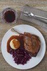 Leg of goose with red cabbage, dumplings and demi glace  on white plate  over wooden surface — Stock Photo