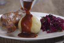 Leg of goose with red cabbage and dumpling with demi glace being poured over the dumpling — Stock Photo