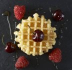 Close-up vista superior de waffle belga com cerejas, framboesas e xarope de bordo — Fotografia de Stock