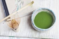 Vista de perto do chá Matcha em uma tigela perto de batedor de bambu e colher — Fotografia de Stock