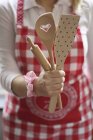 Cropped view of a woman wearing a red and white apron holding a wooden kitchen tools — Stock Photo