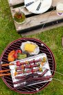 Sausages and vegetables on a charcoal grill outdoors over green grass — Stock Photo