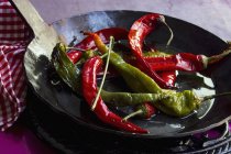 Chiles rojos y verdes fritos en aceite de oliva en una sartén de hierro fundido negro - foto de stock