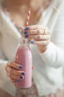 Closeup cropped view of woman holding a glass bottle of vegan raspberry milk shake — Stock Photo