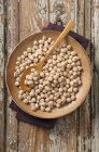 Chickpeas on brown plate with spoon over wooden surface — Stock Photo