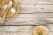 Хумус в миске и на тарелке с ложкой, чесноком и горохом над деревянной поверхностью с тарелками — стоковое фото