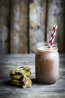 Closeup view of chocolate milk in jar with straw and cookies — Stock Photo