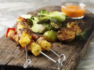Grilled chicken skewers with lemons and vegetables on a wooden board — Stock Photo