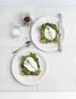 Toast topped with young spinach and poached egg on white plates with fork and knife — Stock Photo