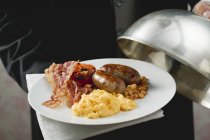 Person holding English breakfast on plate with dome cover — Stock Photo