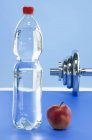 Крупним планом пляшка мінеральної води з яблуком і гантелі — стокове фото