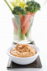 Carrot dip and raw vegetables in glass over white surface — Stock Photo