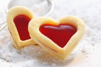 Closeup view of sweet pastry hearts with raspberry jam on icing sugar — Stock Photo