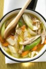 Chicken soup with vegetables in saucepan over white surface — Stock Photo
