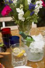 Підвищений вид на біле вино з лимонною водою, квітами та келихами на столі — стокове фото